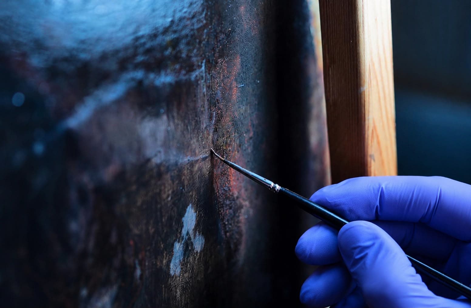 Art conservator using a fine brush to restore details on a historic oil painting canvas
