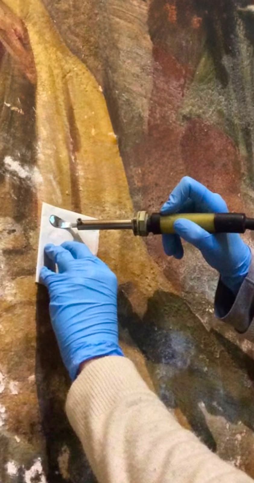 A heated spatula tool used to consolidate a painting's surface at the studio bench