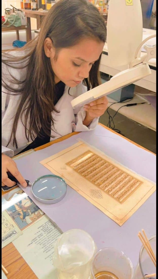 Examining a manuscript folio under a magnifier and hand loupe
